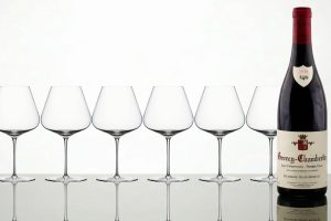 Bouteille de vin Gevrey-Chambertin 1er Cru Les Champonnets 2018 accompagnée de six verres à Bourgogne vides.